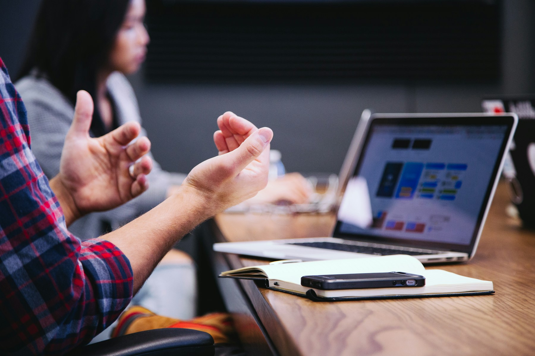 Hands gesturing beside a laptop and notebook during a meeting